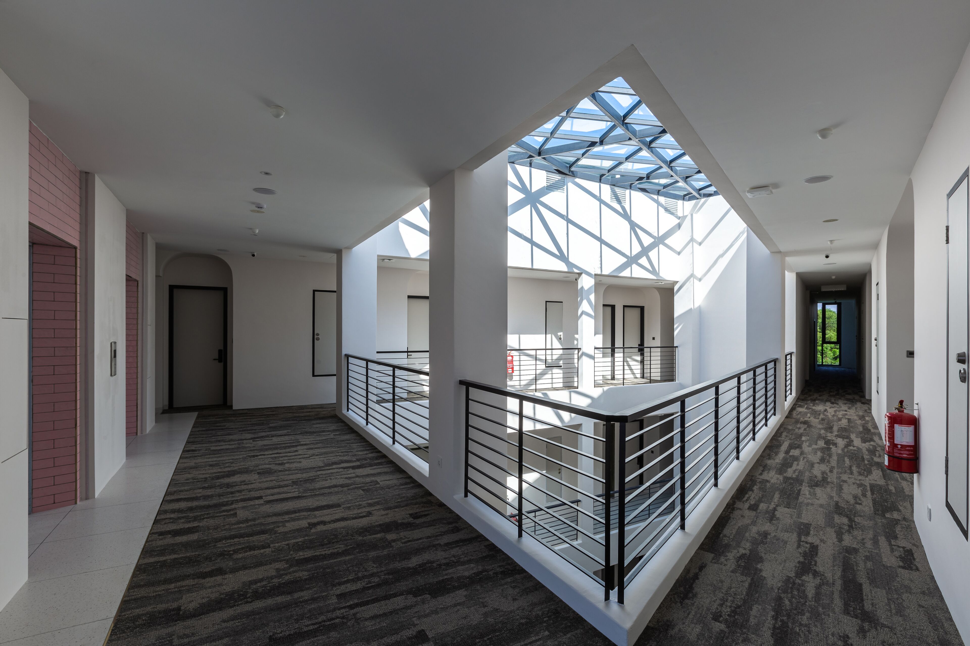A spacious corridor with a high ceiling, a glass skylight, and a fire extinguisher on the right.