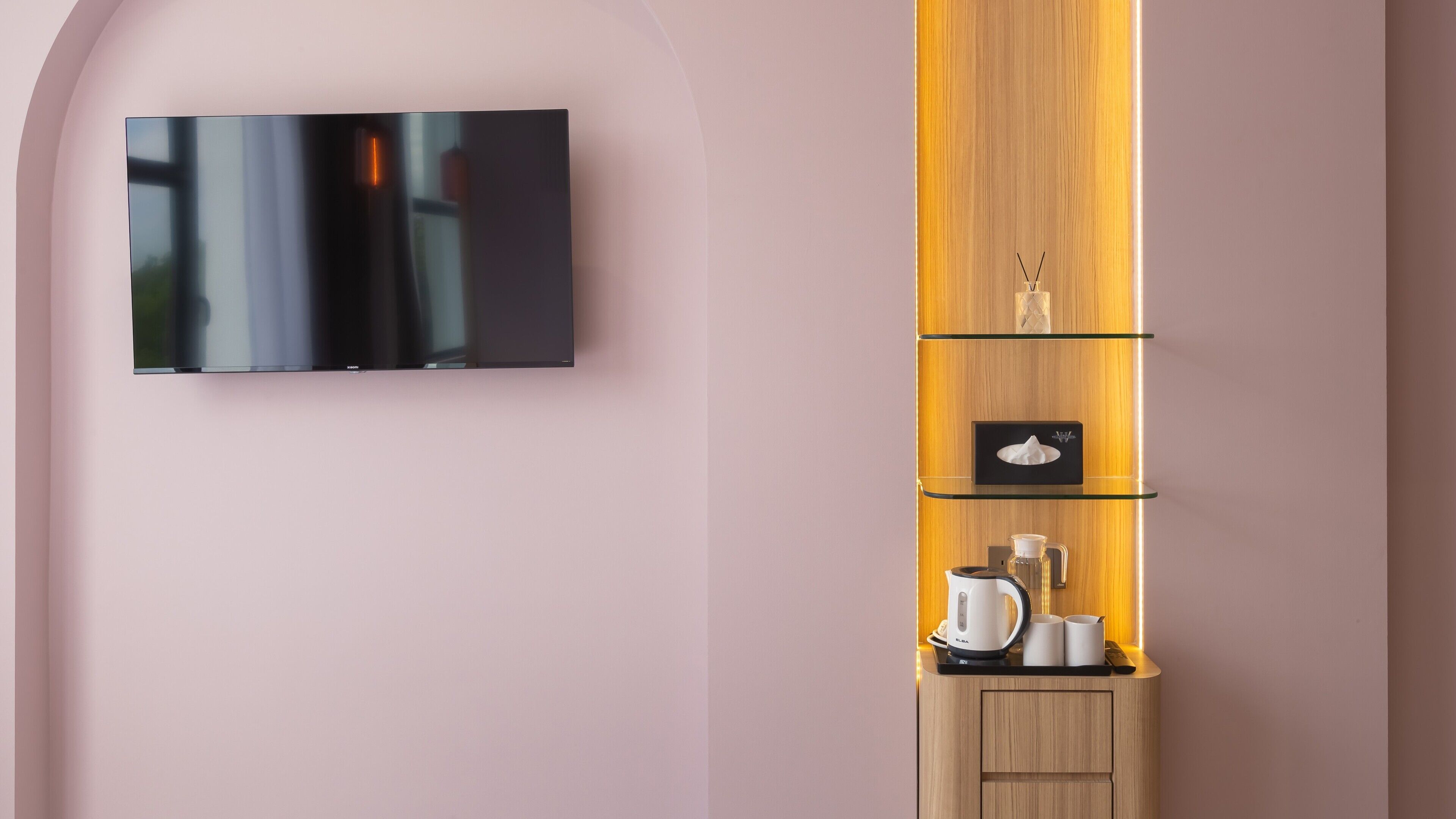 A modern room with a flat-screen TV mounted on the wall, a wooden cabinet with glass shelves, and a coffee maker.