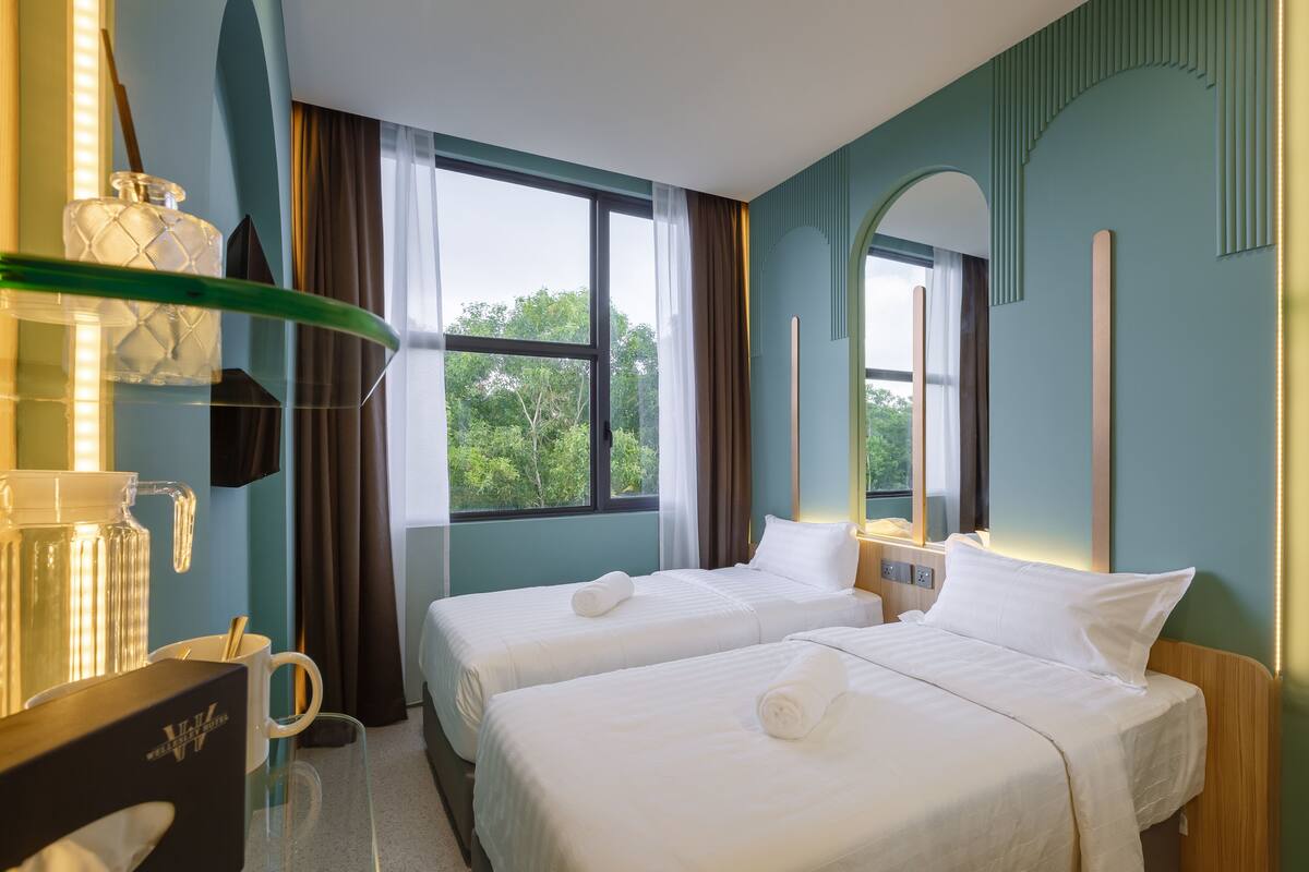 A hotel room with two beds, a glass coffee table, a minibar, and a large window with curtains.