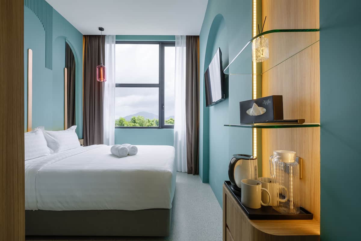 A hotel room with a bed, a coffee station, a TV, and a window with a view of greenery.