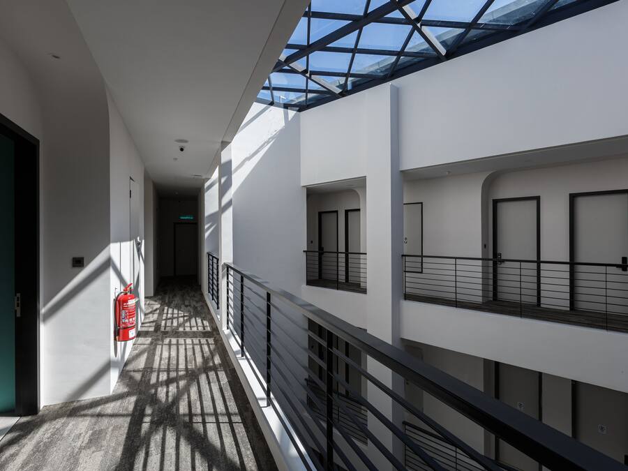 Un interior moderno con techo de vidrio, un extintor y un pasillo que lleva a varias puertas.