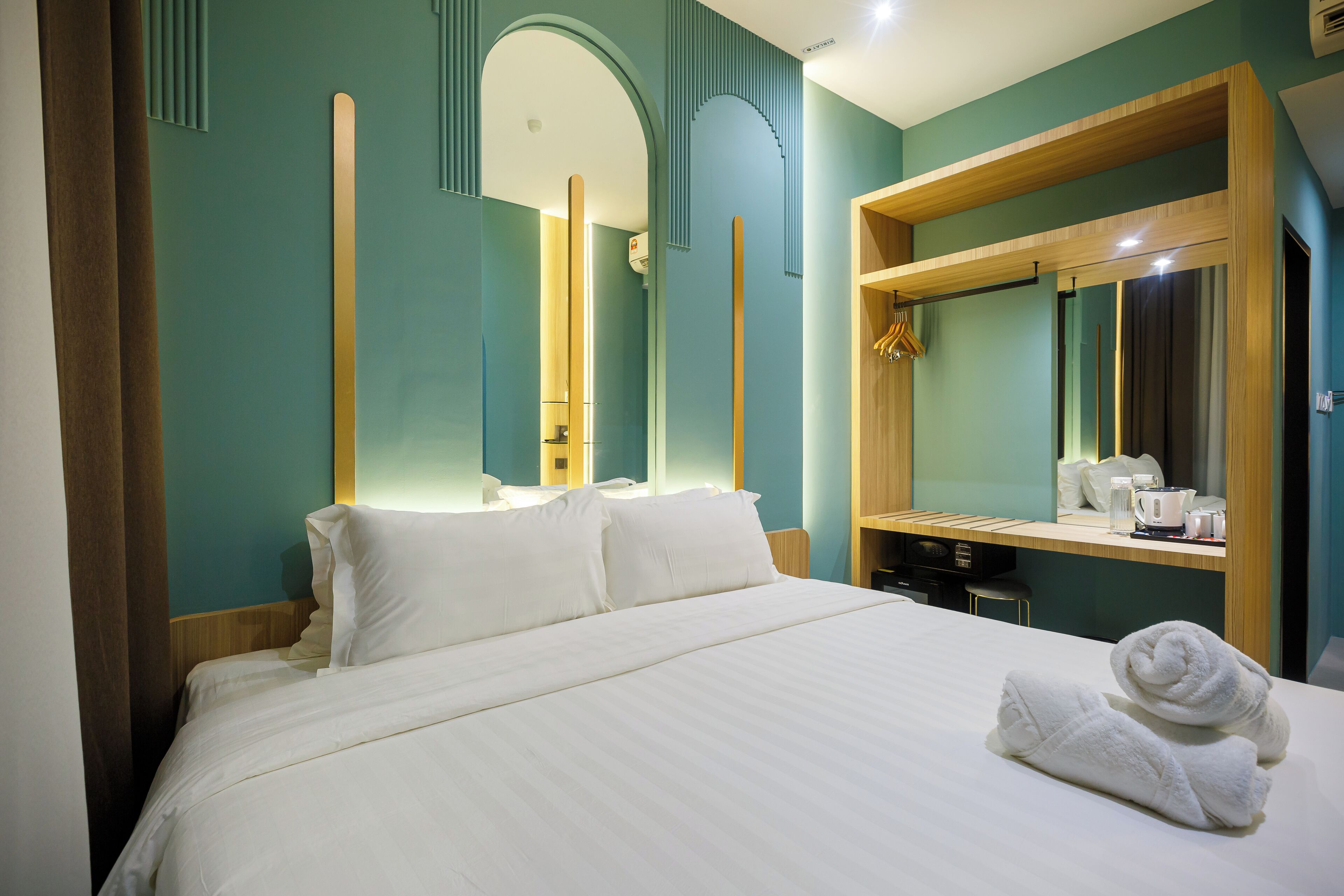A hotel room with a large bed, a wooden headboard, a mirror, and a small desk with a kettle and cups.