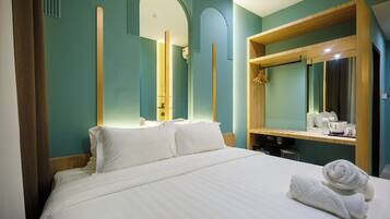 Quarto de hotel com uma cama grande, cabeceira de madeira, espelho e uma pequena escrivaninha com chaleira e chávenas.