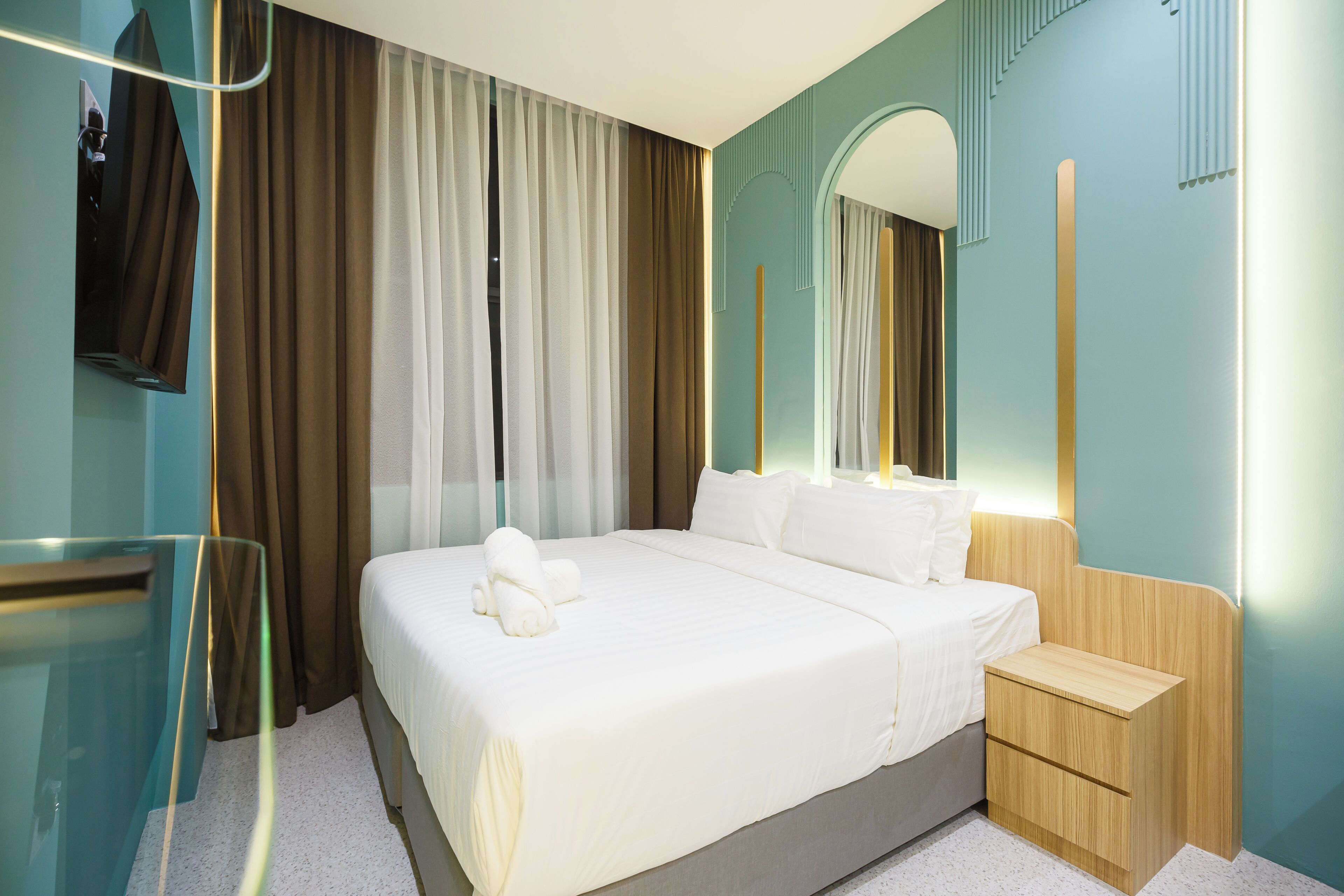A hotel room with a large bed, a wooden nightstand, a mirror, and a TV mounted on the wall.