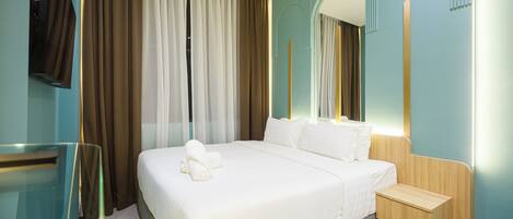 A hotel room with a large bed, a wooden nightstand, a mirror, and a TV mounted on the wall.
