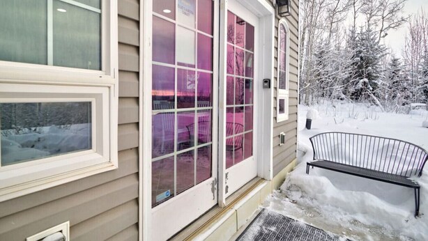 Una casa con puerta principal, una ventana y un banco cubiertos de nieve.