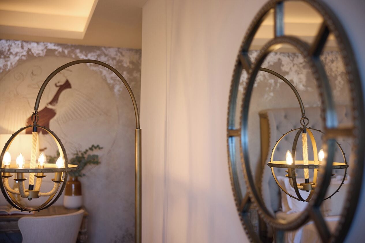 Two ornate chandeliers with multiple candle-like lights, set against a wall with a decorative mirror and a framed artwork.