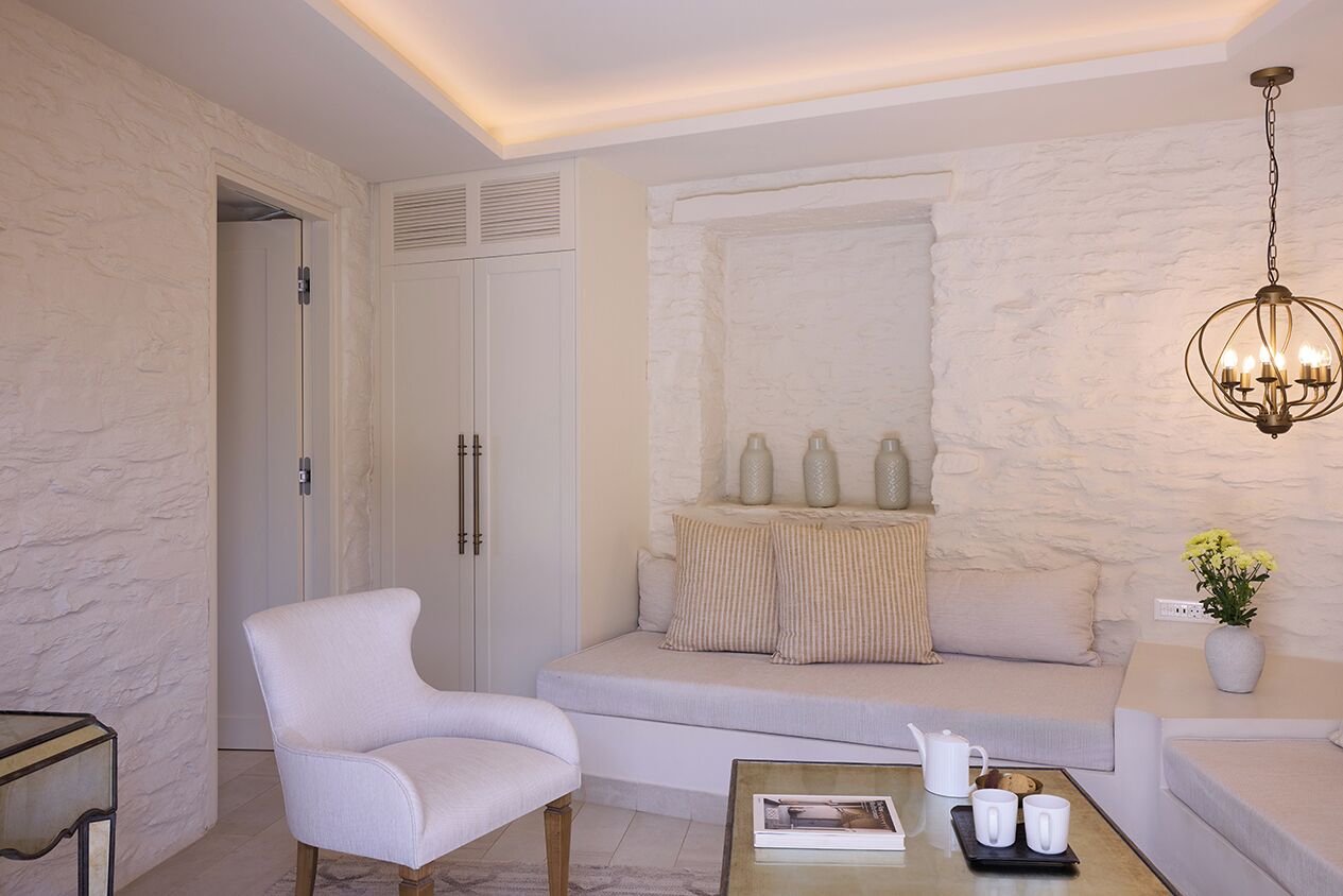 A modern living room with a white sofa, a white armchair, a coffee table with a magazine, and a chandelier.