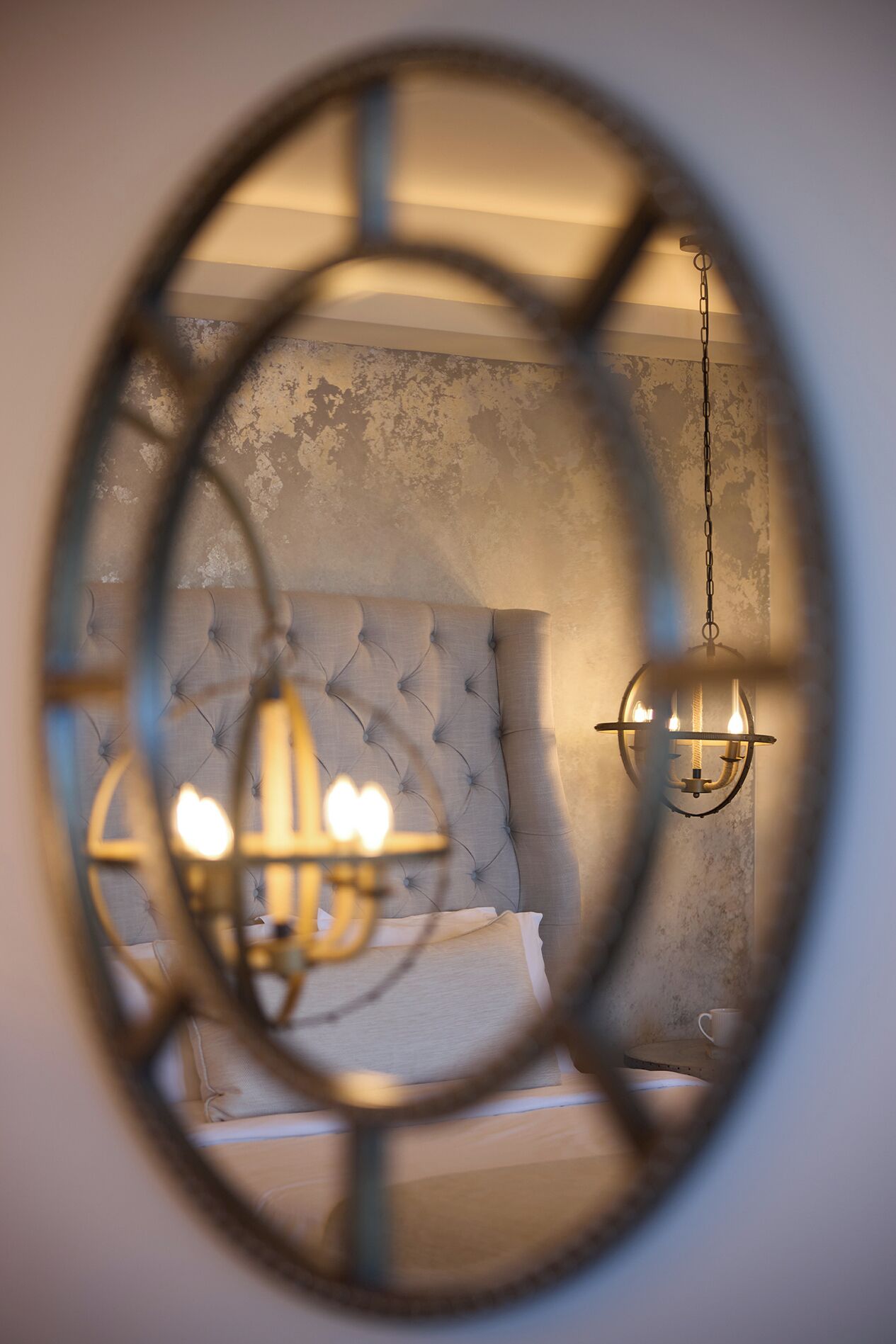 A bedroom with a tufted headboard, a hanging light fixture, and a circular window view.