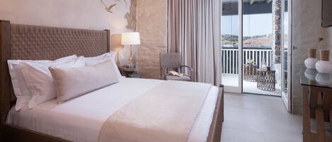 A hotel room with a large bed, a nightstand with a lamp, a chair, a balcony with outdoor furniture, and a TV on a cabinet.