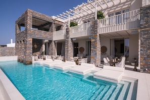 A modern poolside area with a stone facade, outdoor seating, and a clear blue pool.