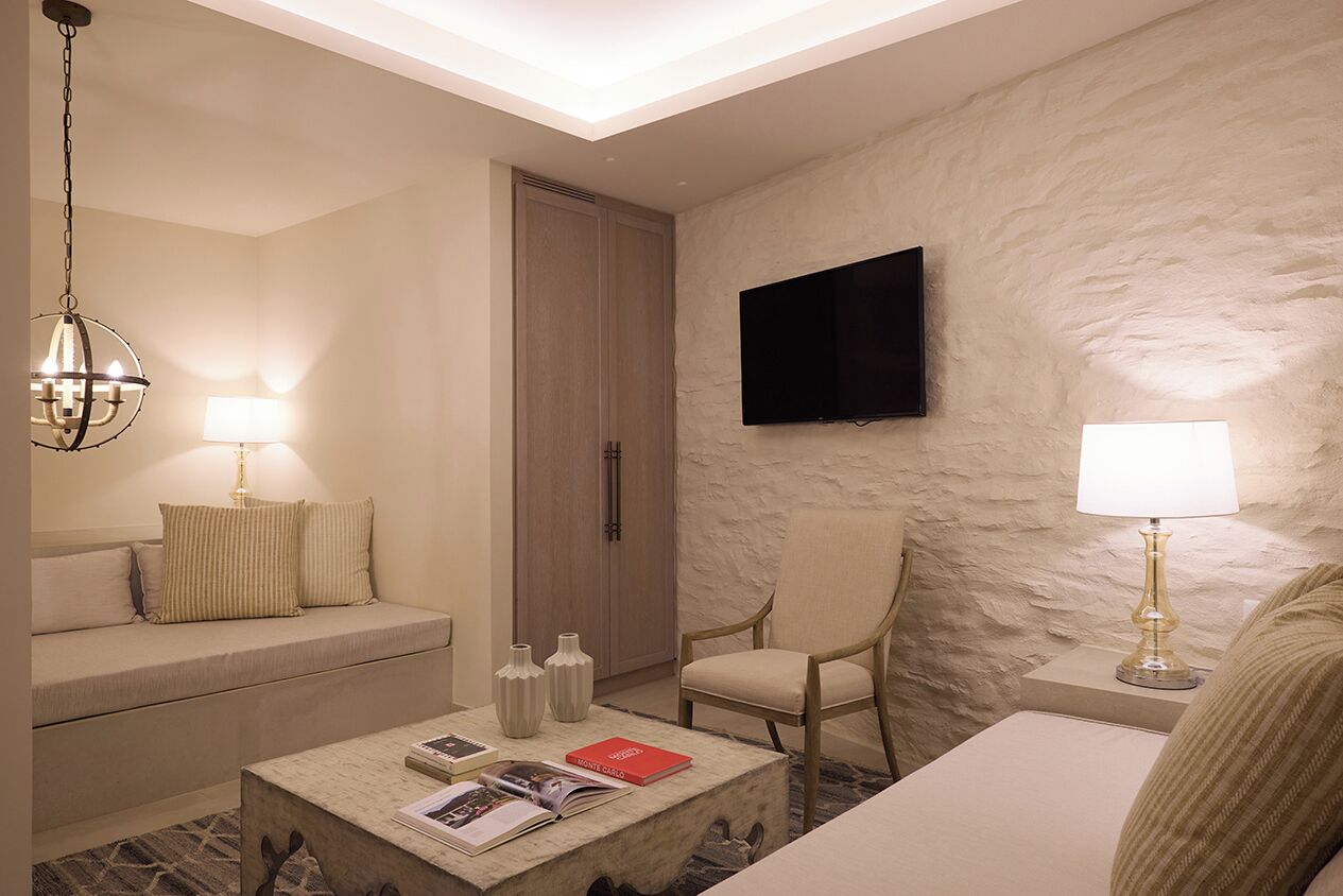 A hotel room with a sofa, armchair, coffee table, TV, and a stone-textured wall.