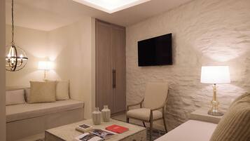 A hotel room with a sofa, armchair, coffee table, TV, and a stone-textured wall.