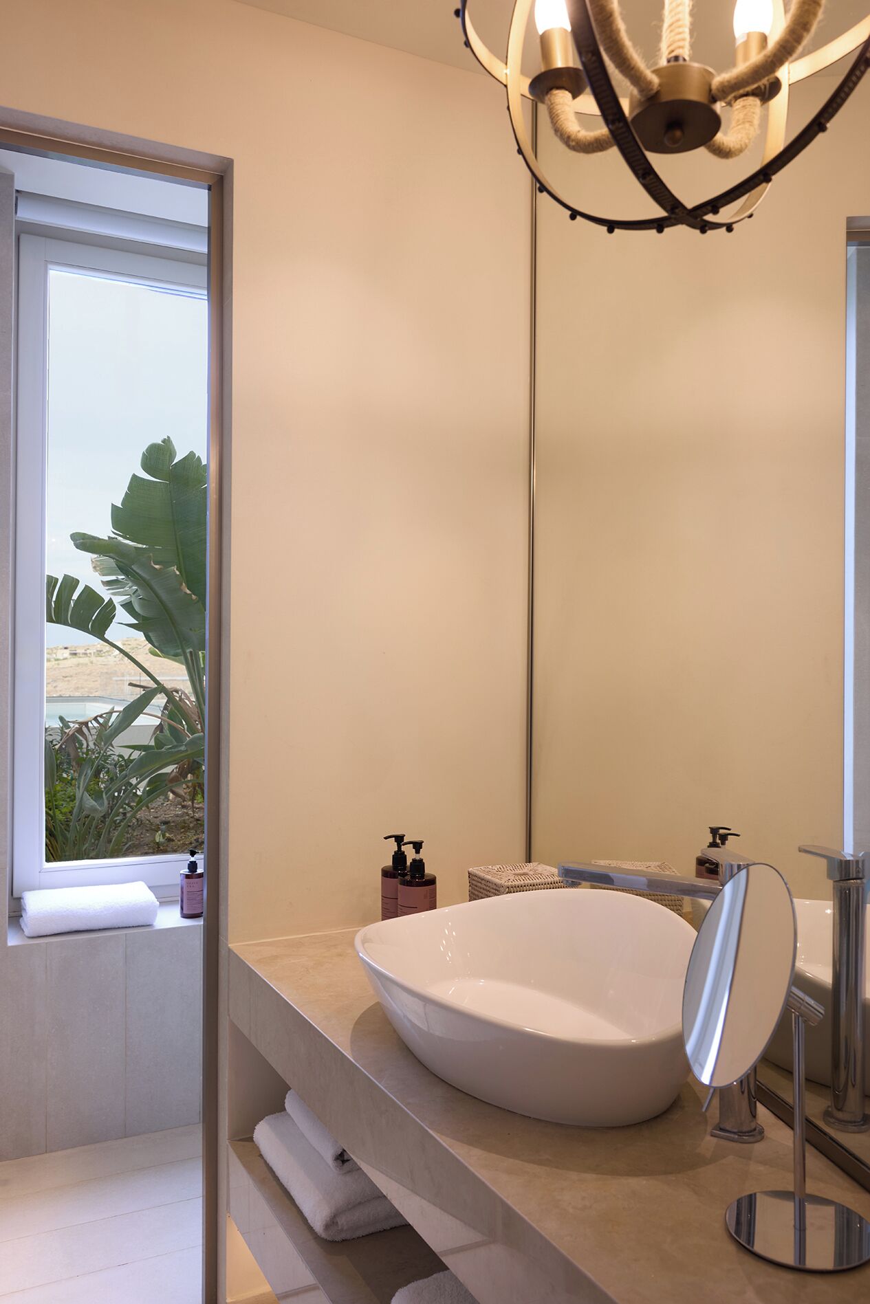 Un baño moderno con un lavamanos ovalado grande, un espejo y una ventana con vista a la vegetación.