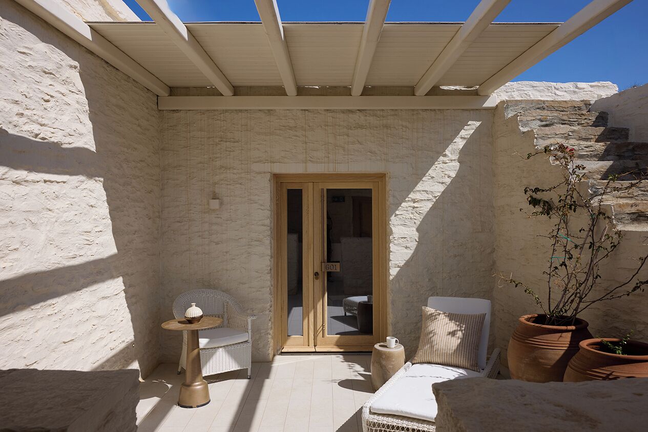 A sunlit patio with a white chair, a small table, and a potted plant.