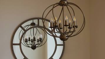 A dining area with a round table, chairs, a chandelier, and a large mirror on the wall.