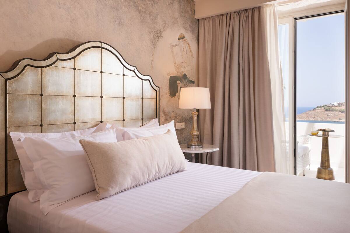 Een hotelkamer met een groot bed, een hoofdeinde, een lamp en uitzicht op zee.