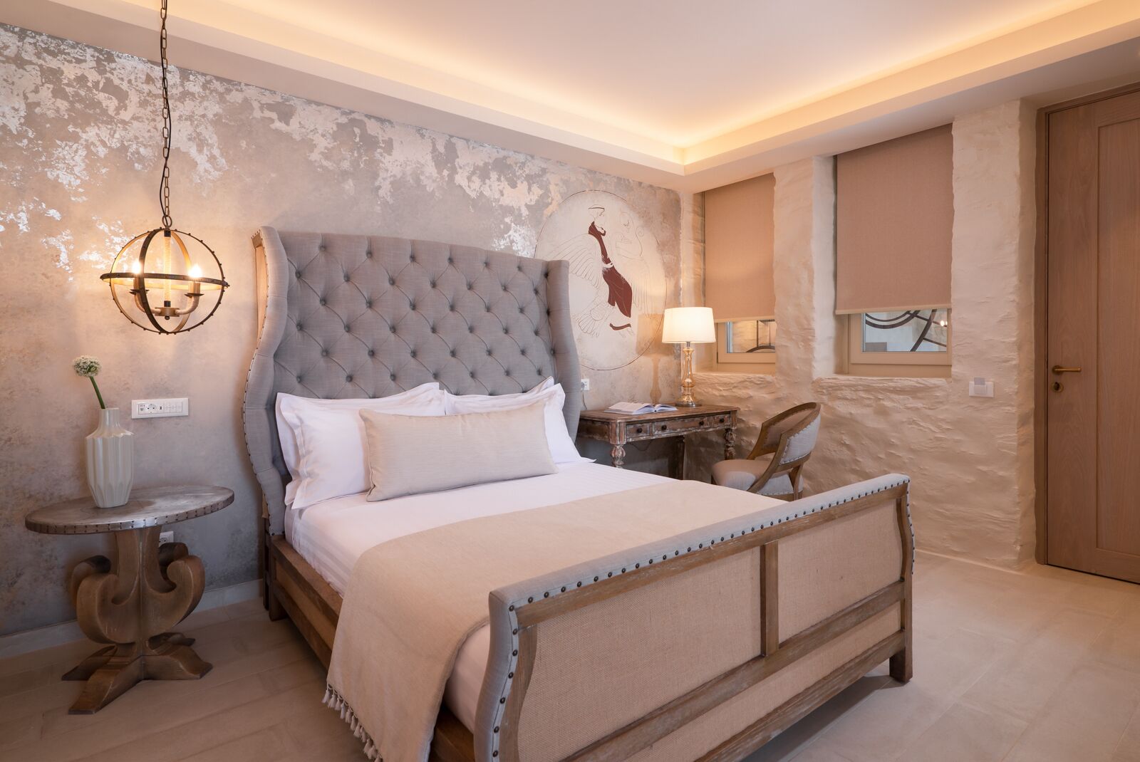 A bedroom with a tufted headboard, a round bedside table, a chair, and a lamp.