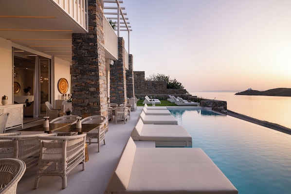 A poolside area with lounge chairs and a stone wall, overlooking a calm body of water.