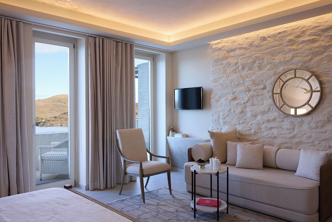 A hotel room with a bed, a sofa, a chair, a television, and a stone wall.