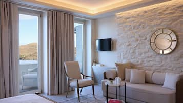 A hotel room with a bed, a sofa, a chair, a television, and a stone wall.