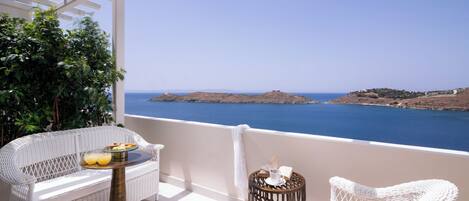 A balcony with wicker furniture, a table with drinks, and a view of the sea and islands.