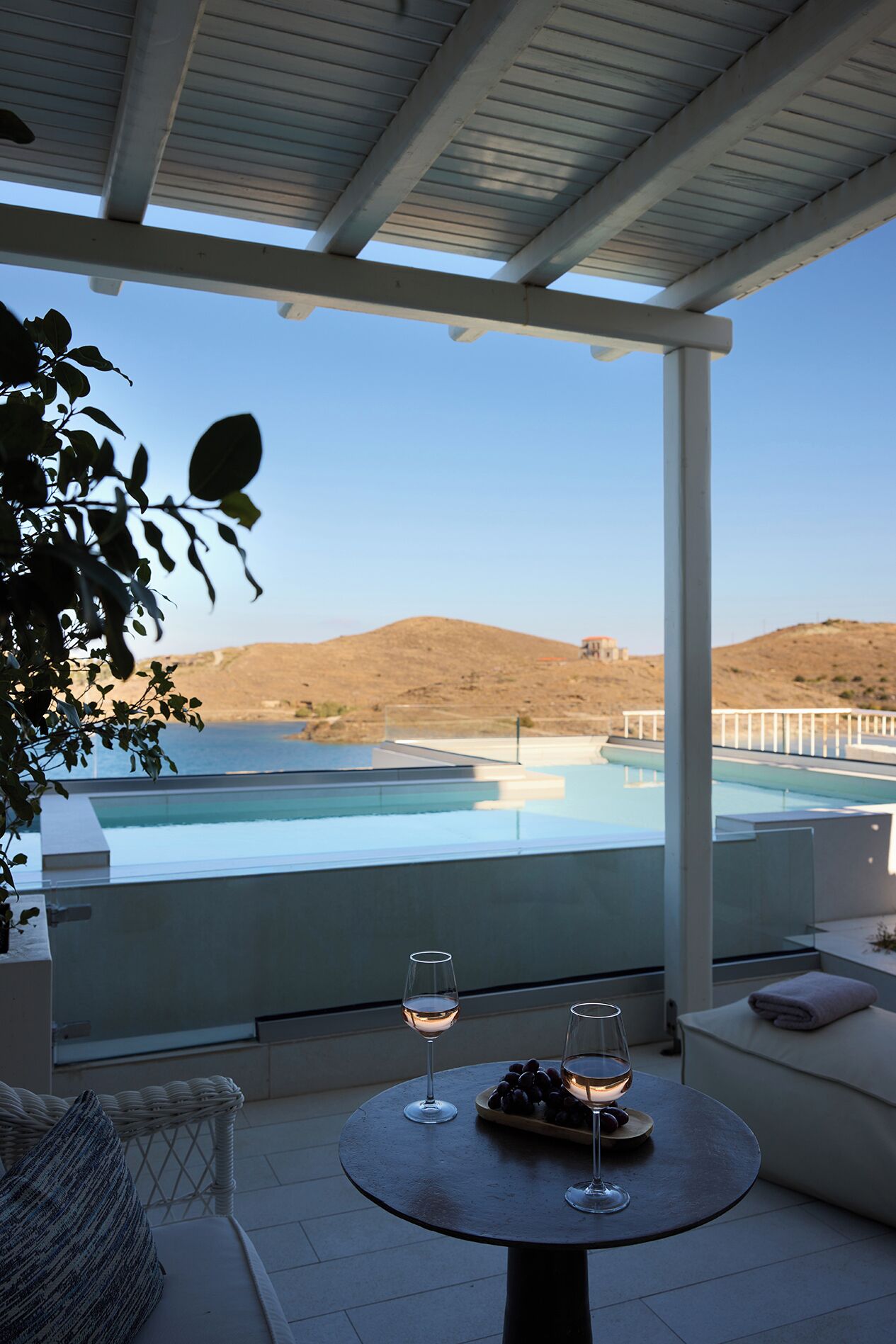 A balcony with a pool view, two glasses of wine, and a wicker chair.