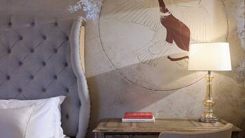 A hotel room with a tufted headboard, a bed with white linens, a desk with a lamp, and a wall mural.