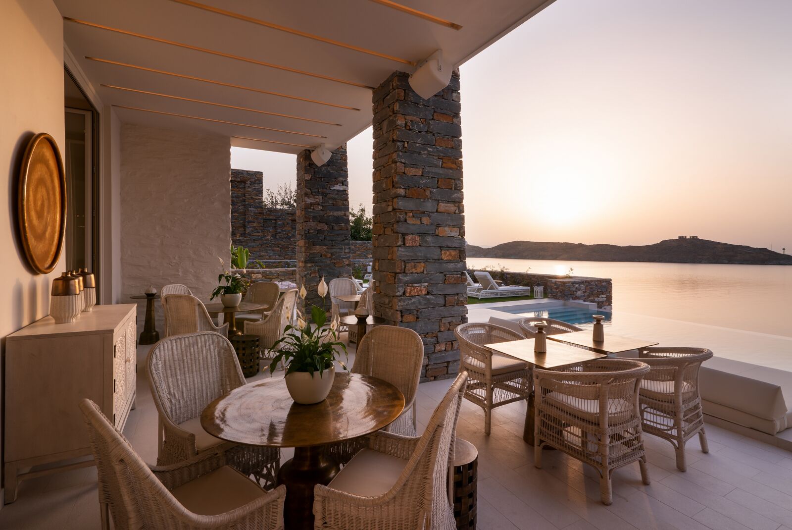 A terrace with wicker furniture, a round table with a potted plant, and a stone wall.