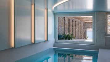 A modern indoor swimming pool with a curved ceiling and a view of an outdoor stone wall.