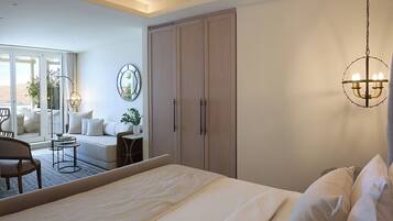 A bedroom with a large bed, a wardrobe, a chandelier, and a view of a balcony with outdoor furniture.
