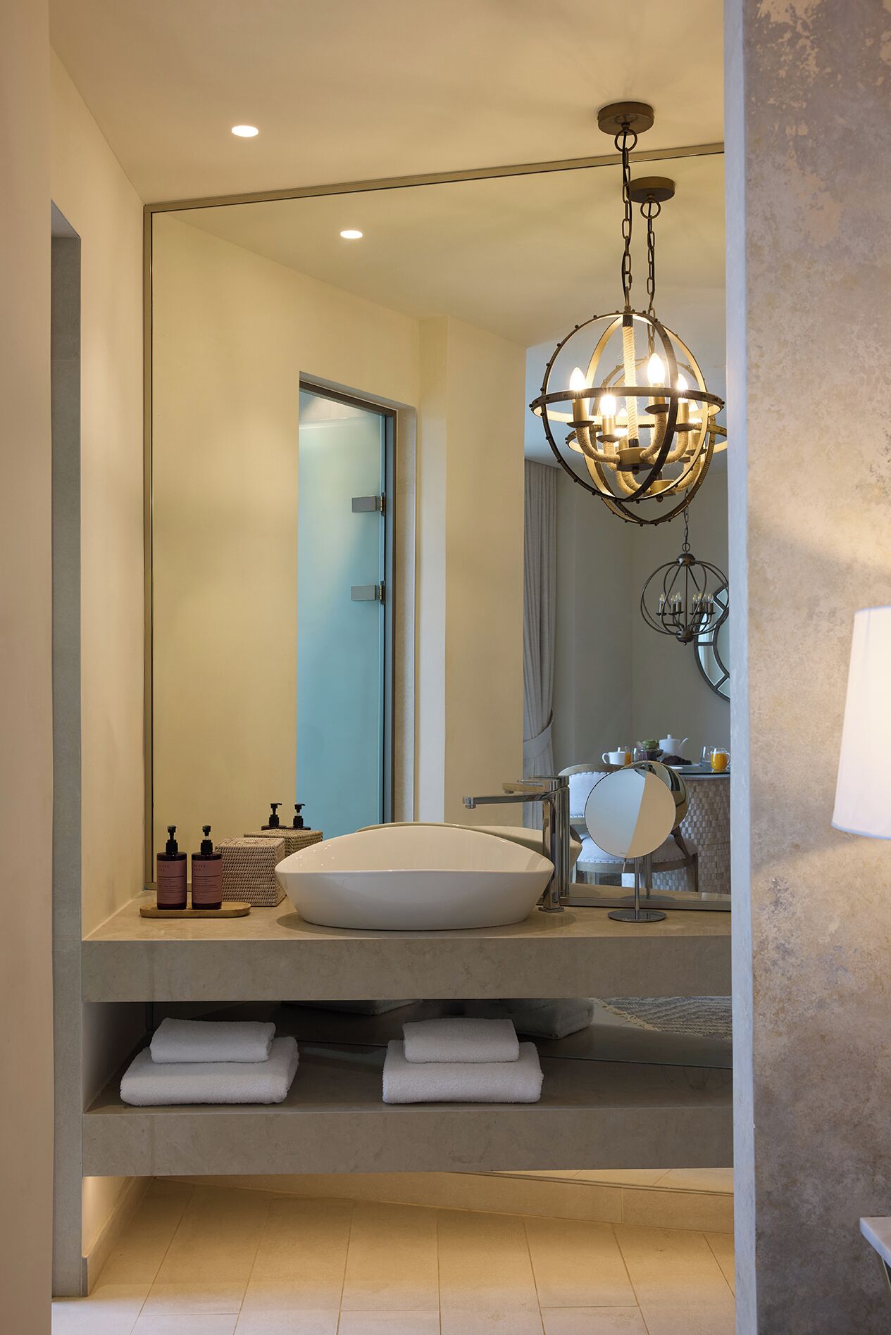 A modern bathroom with a large mirror, a round sink, and a chandelier.