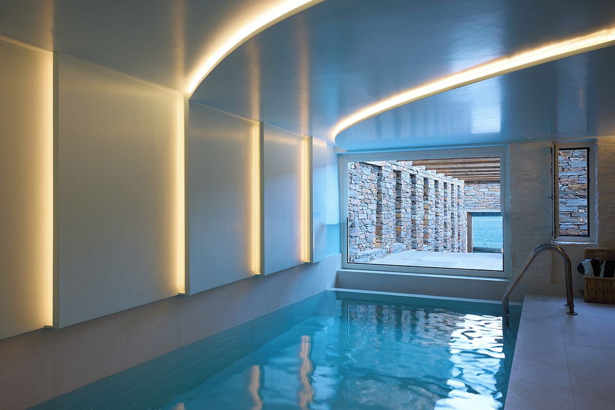 A modern indoor swimming pool with a stone wall and a view of the sea.