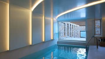 A modern indoor swimming pool with a stone wall and a view of the sea.