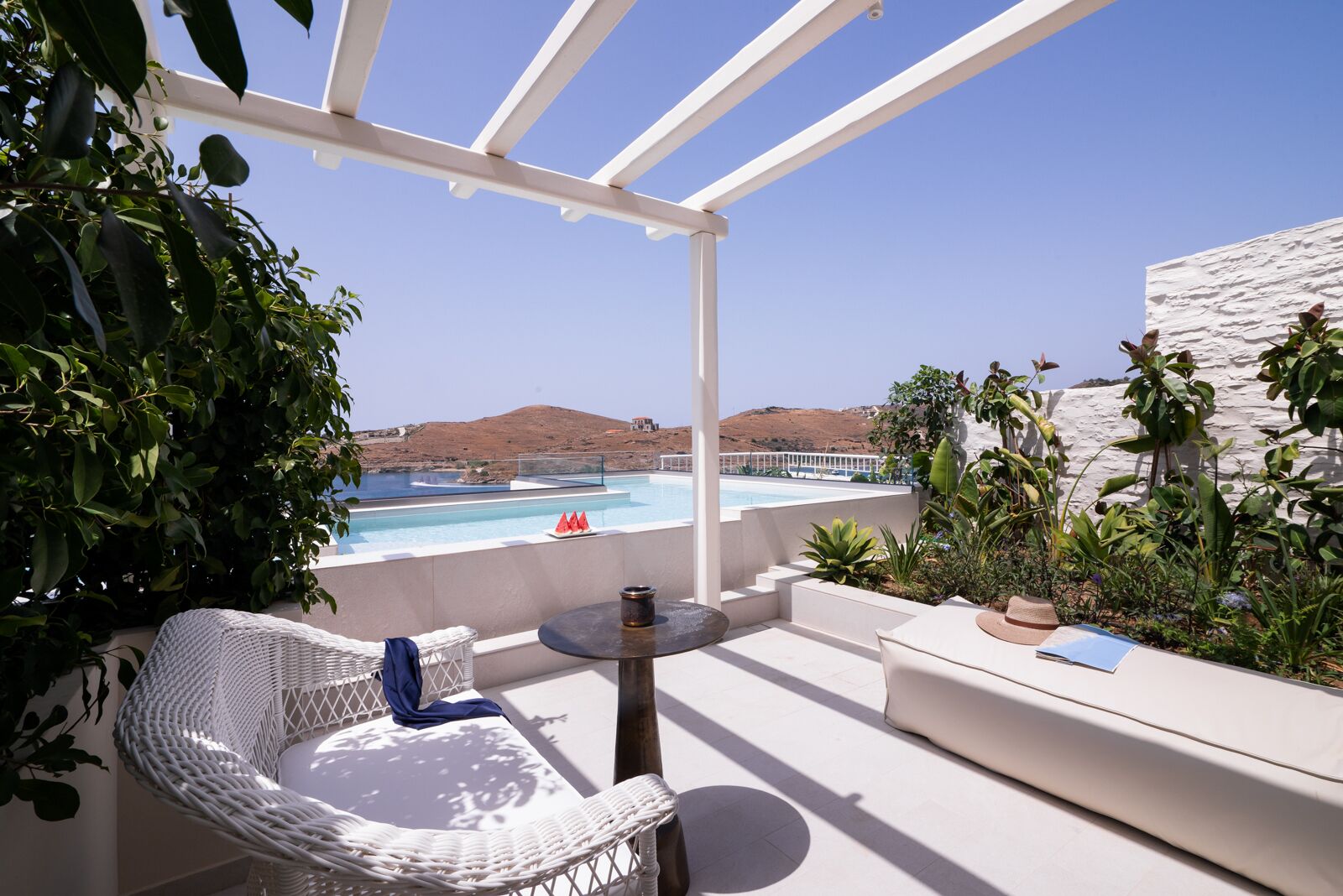 A terrace with a white pergola, a pool, and a view of the sea.