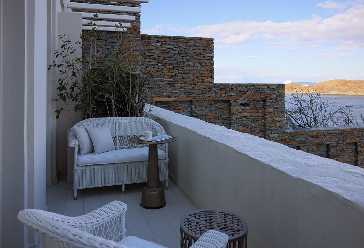 Un balcon agrémenté de meubles en osier, un mur en pierre et une vue sur l’eau.