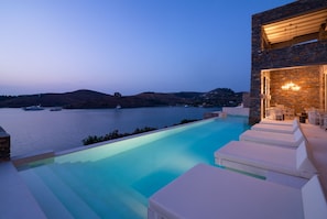 A poolside area with lounge chairs, a stone wall, and a view of the water and hills.