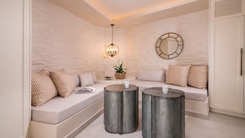 A modern living room with a white stone wall, a round mirror, a hanging light fixture, a sofa with cushions, and two round metal side tables.