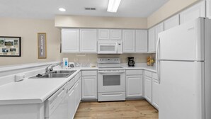 Une cuisine moderne avec des meubles blancs, un four à micro-ondes encastré, une cuisinière et un réfrigérateur.
