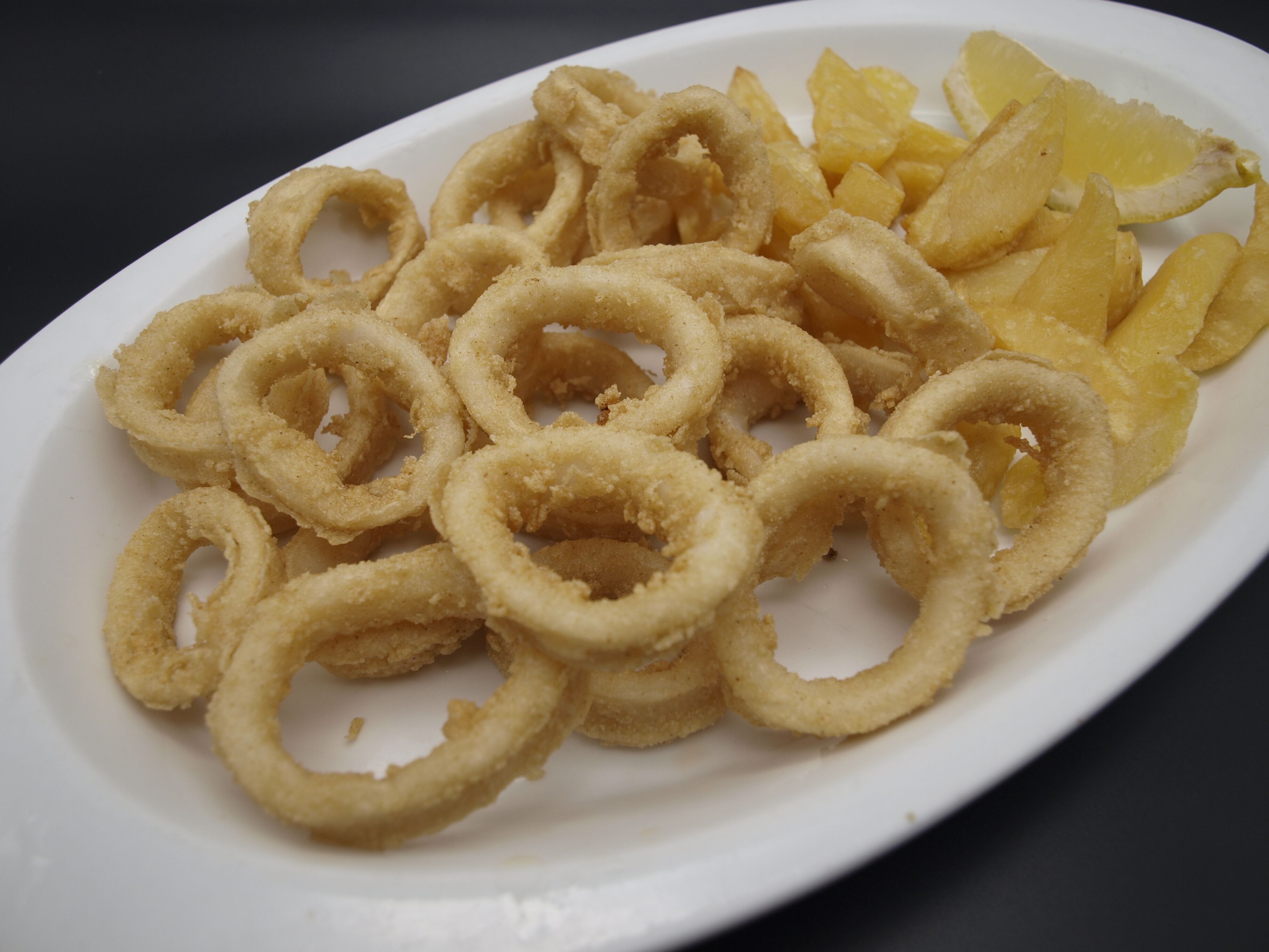 Un plato de aros de calamares fritos y gajos de limón.