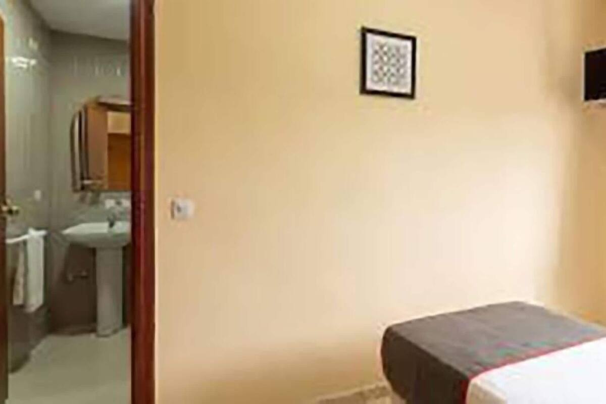 Ein Zimmer mit einem Bett, einem kleinen Tisch, einem an der Wand befestigten Regal und einer Tür zu einem Badezimmer.