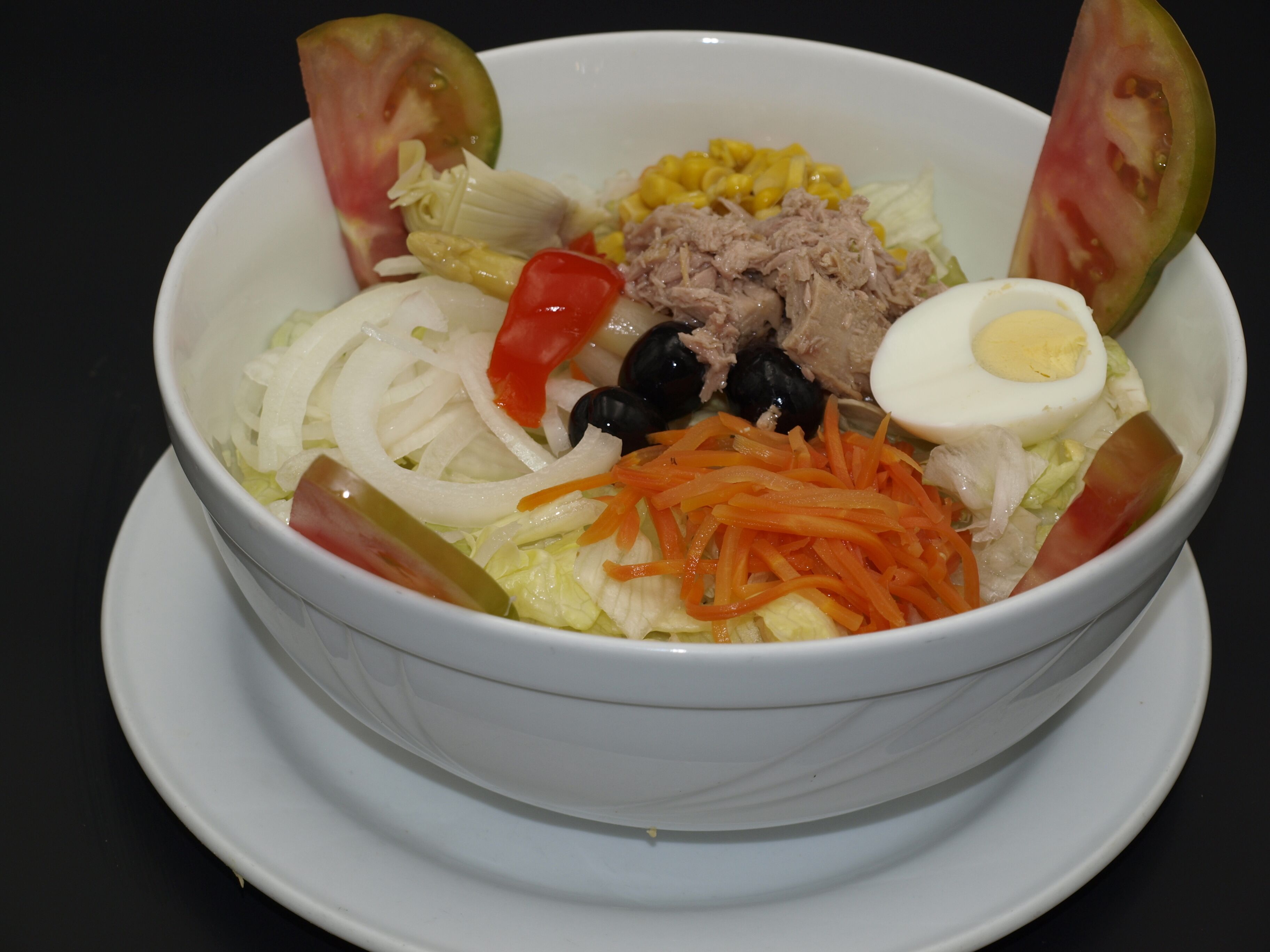 A bowl of salad with various ingredients like lettuce, tomatoes, carrots, and a boiled egg.
