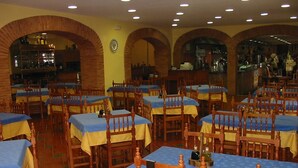 A restaurant with multiple tables and chairs, brick arches, and a bar area. - Hostal Restaurante Asador EL PAISANO (Utrera)