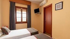 A hotel room with two beds, a window with curtains, a door, and a flat-screen TV mounted on the wall. - Hostal Restaurante Asador EL PAISANO (Utrera)