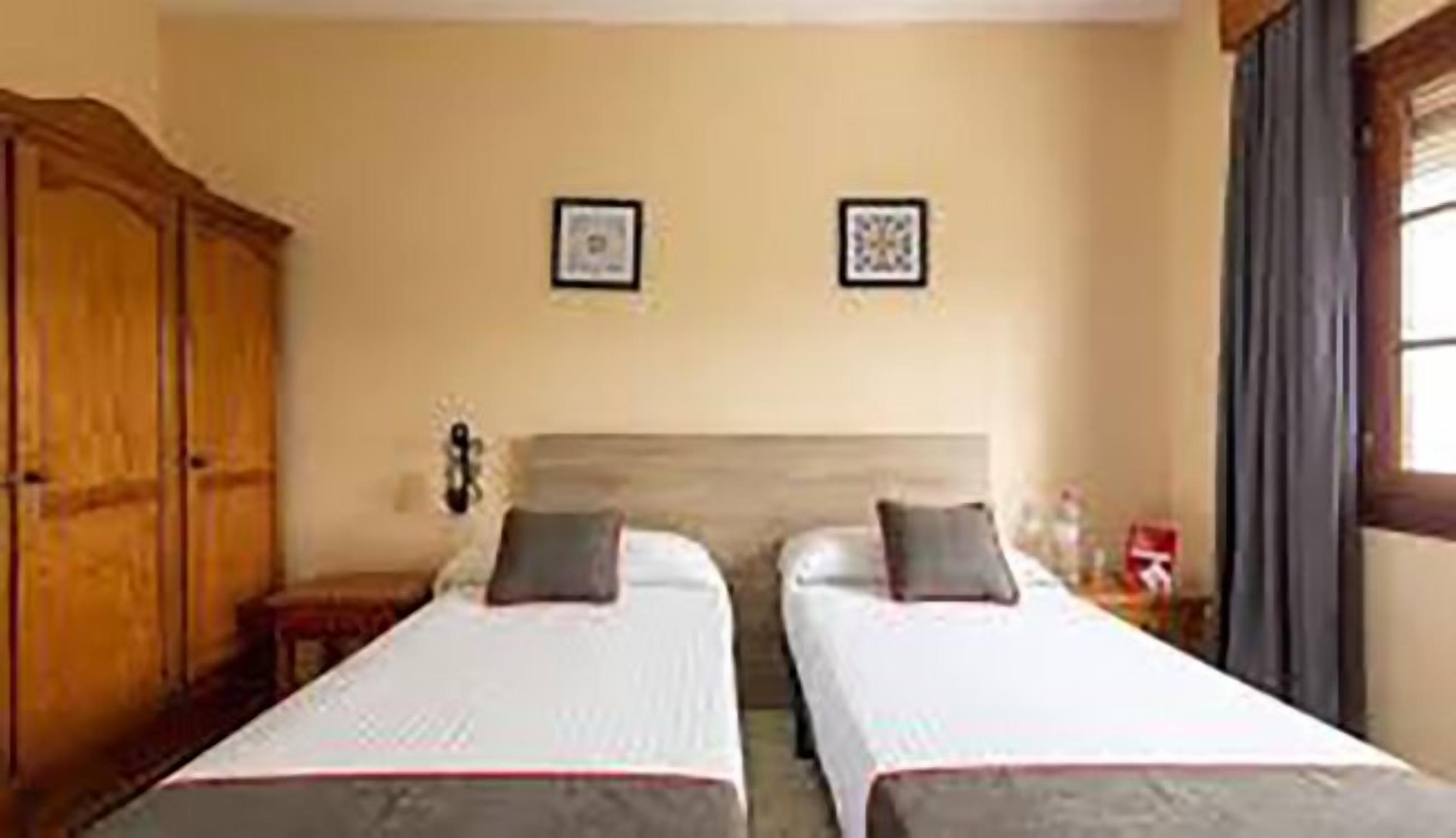 A hotel room with two single beds, a wooden wardrobe, and a window with curtains.