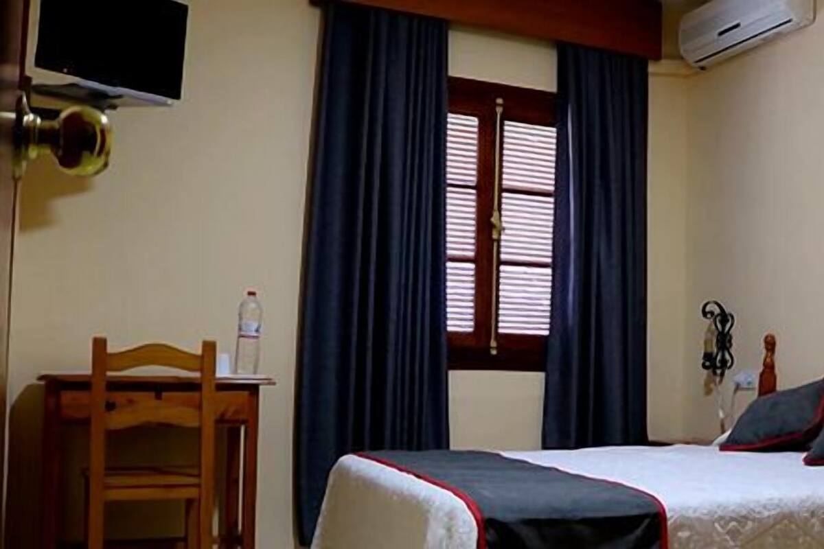 Ein Schlafzimmer mit einem Bett, einem Schreibtisch, einem Stuhl, einem Fernseher und einer Klimaanlage.