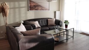 A modern living room with a leather sofa, a glass coffee table, and a large window with sheer curtains. - Schaake Hooksiel to feel good with 76sqm & balcony (Wangerland)