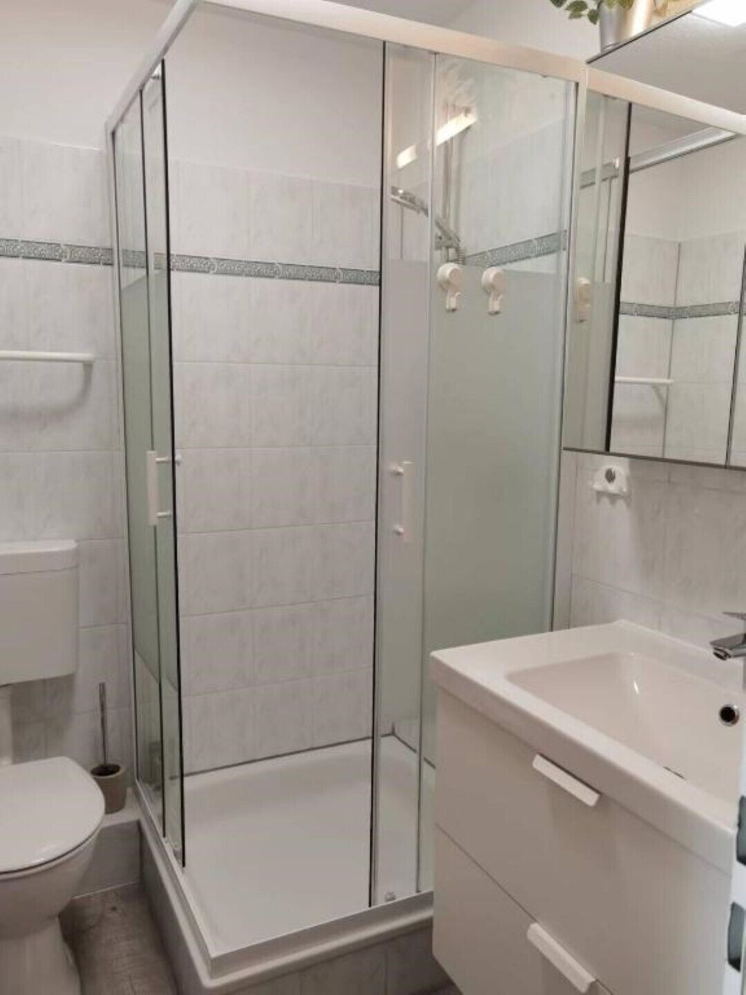 Un baño moderno con cabina de ducha de vidrio, un lavamanos blanco y un inodoro.