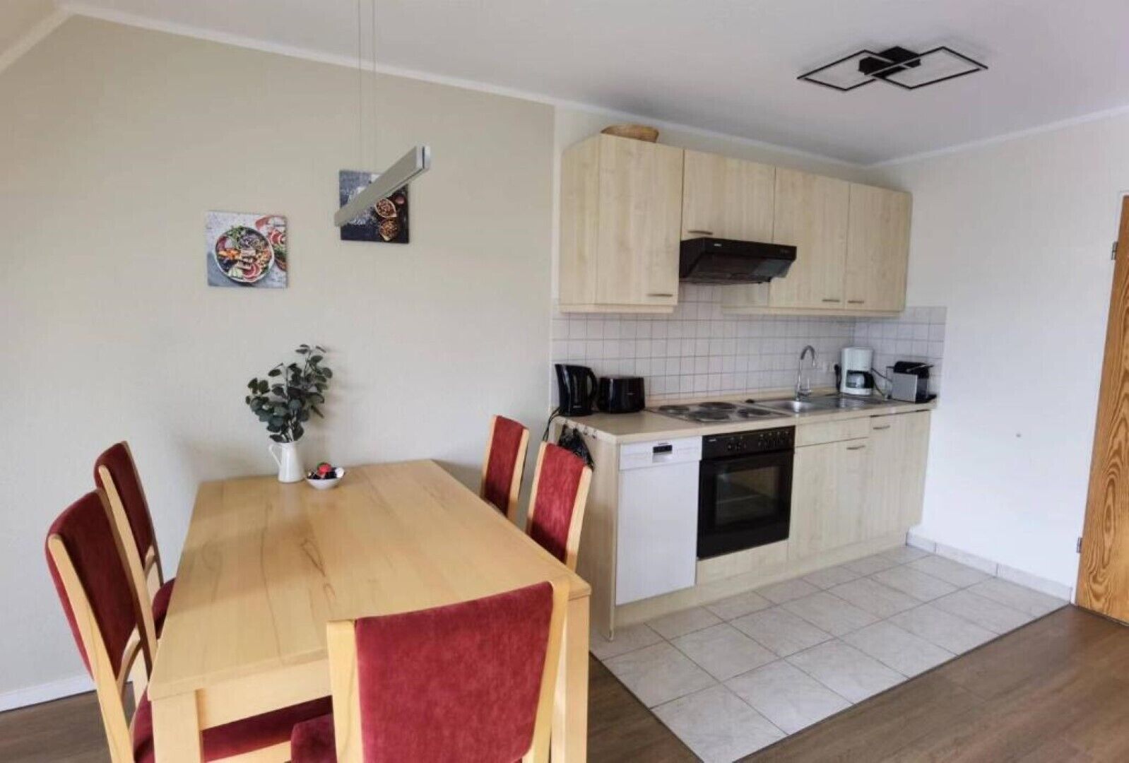 Cocina compacta con comedor, que incluye una mesa de madera, sillas rojas, lavavajillas y estufa.