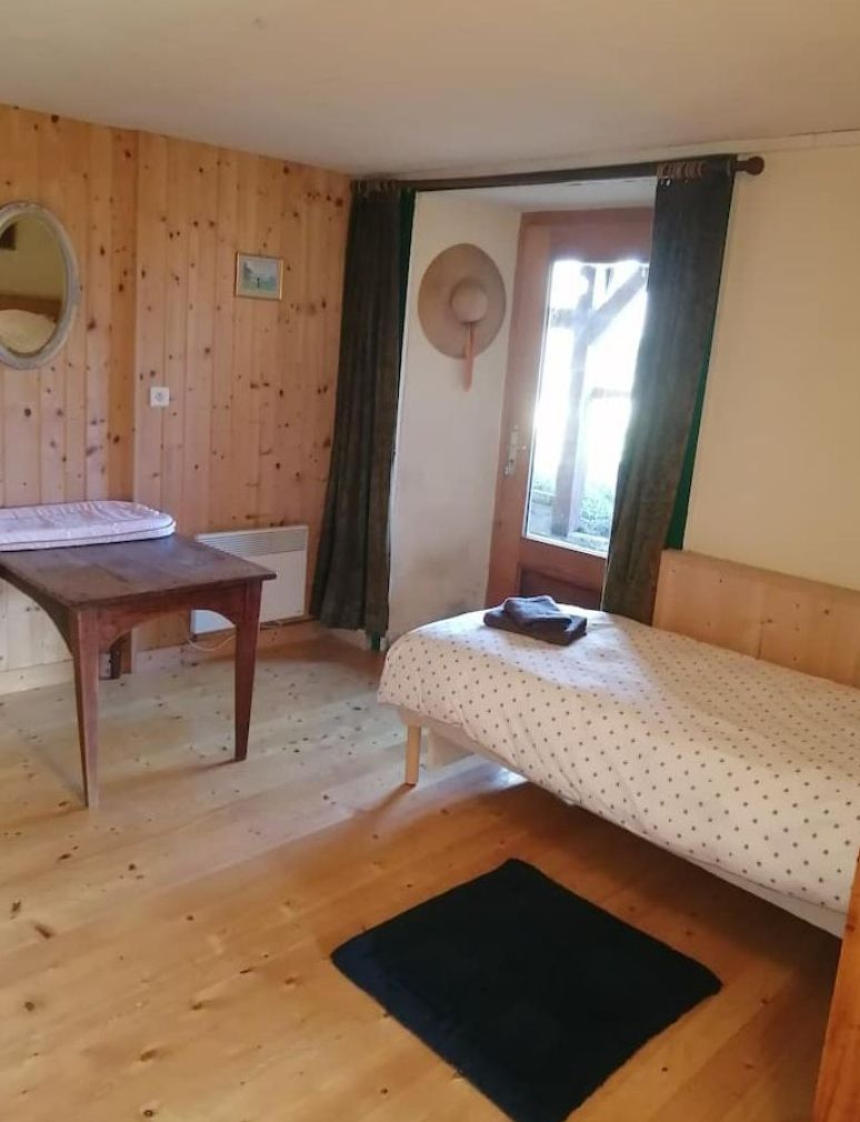 Une pièce avec un plancher en bois, un lit avec un matelas blanc et une couverture à pois, une table en bois, un miroir et une fenêtre avec des rideaux.
